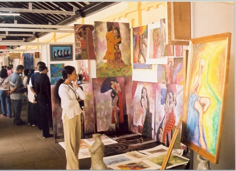 Several people engaged in observing and discussing paintings showcased in an exhibition space.